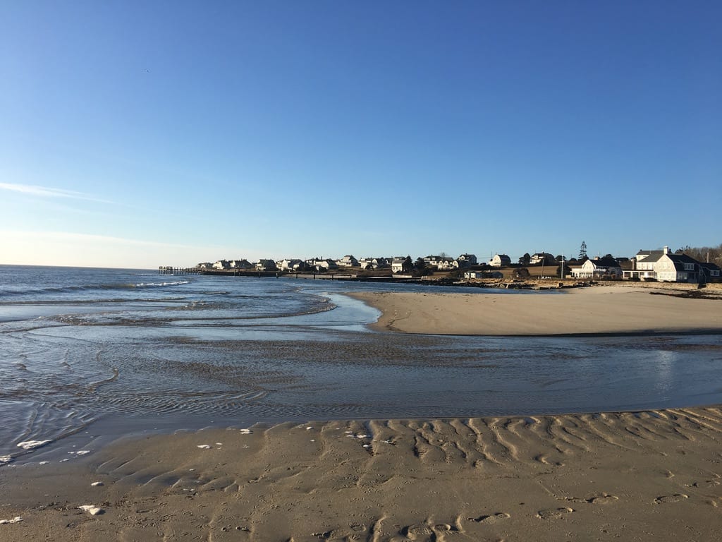 Low tide at a Dartmouth beach, rippled sand and tide pools in front of a row of shingled beach houses under a clear sky.