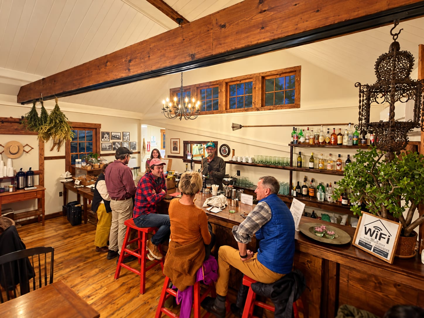 Neighbors on red stools at the wooden bar inside Davoll's, exposed beams and a chandelier above.