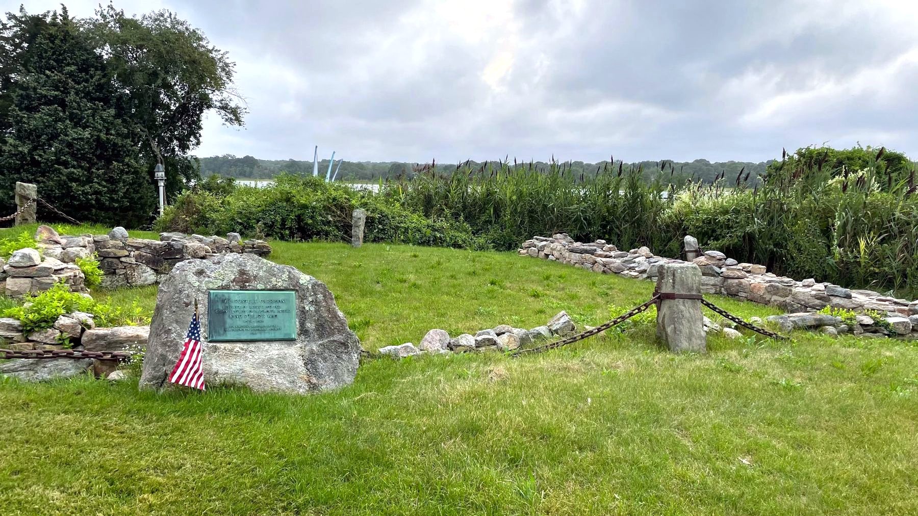 The Russell Garrison site: a bronze plaque on a boulder inside low stone walls, with the Apponagansett marsh behind.
